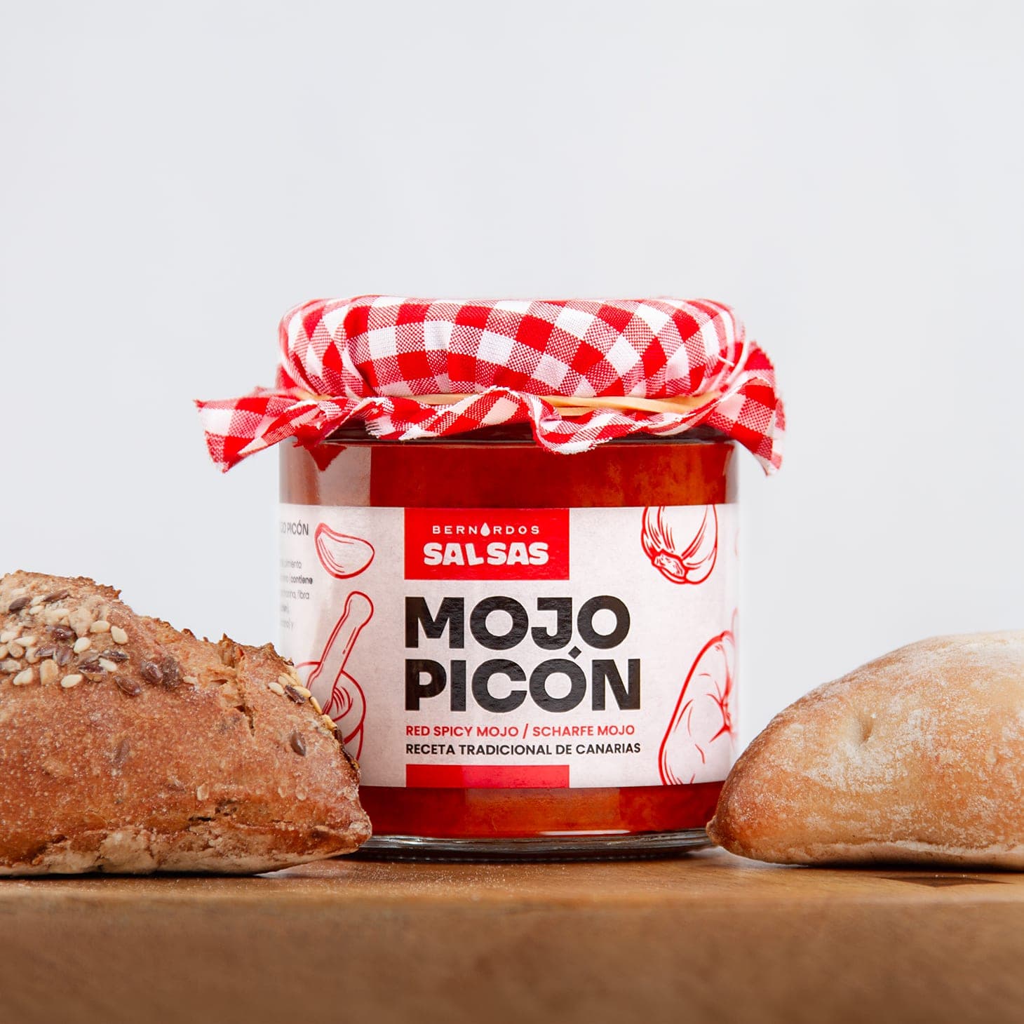 Tarro de mojo picón, con la tela de cuadros atada, sobre una tabla con pan